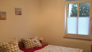 Un dormitorio con cama de madera, ropa de cama roja, una ventana con persianas y dos obras de arte en la pared.