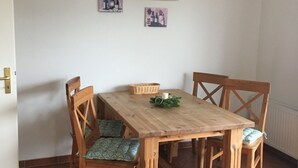 Un comedor con una mesa y sillas de madera, una lámpara colgante y dos cuadros en la pared.