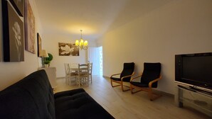 A living room with a sofa, two armchairs, a TV, and a dining area with a table and chairs.