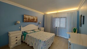 A bedroom with a bed, bedside tables, a dresser, a window with curtains, and a wall-mounted artwork.