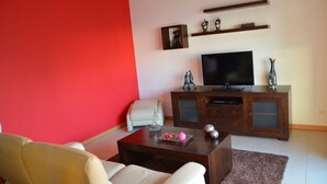 Un salon avec un mur rouge, un téléviseur, un meuble et une table basse.