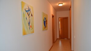Un couloir avec deux tableaux abstraits accrochés aux murs, une porte en bois au fond et un sol carrelé.