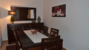 Un coin repas avec une table en bois, des chaises, un saladier de fruits, une lampe, un vase et un tableau accroché au mur.