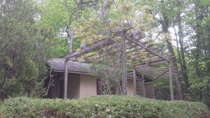 A wooden pergola structure with a sloped roof, surrounded by dense green foliage and trees. - Nature lovers chalet nestled in the heart of Perigord with heated pool (Sagelat - Belvès)