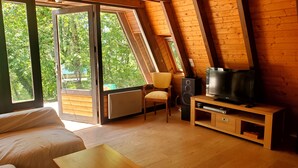 Una habitación acogedora con techo de madera, un sofá, un televisor y una silla.