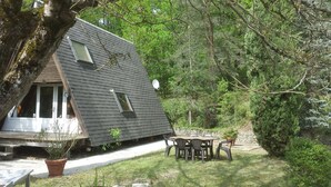 Una casita con techo inclinado, un porche y un patio con mesa y sillas.