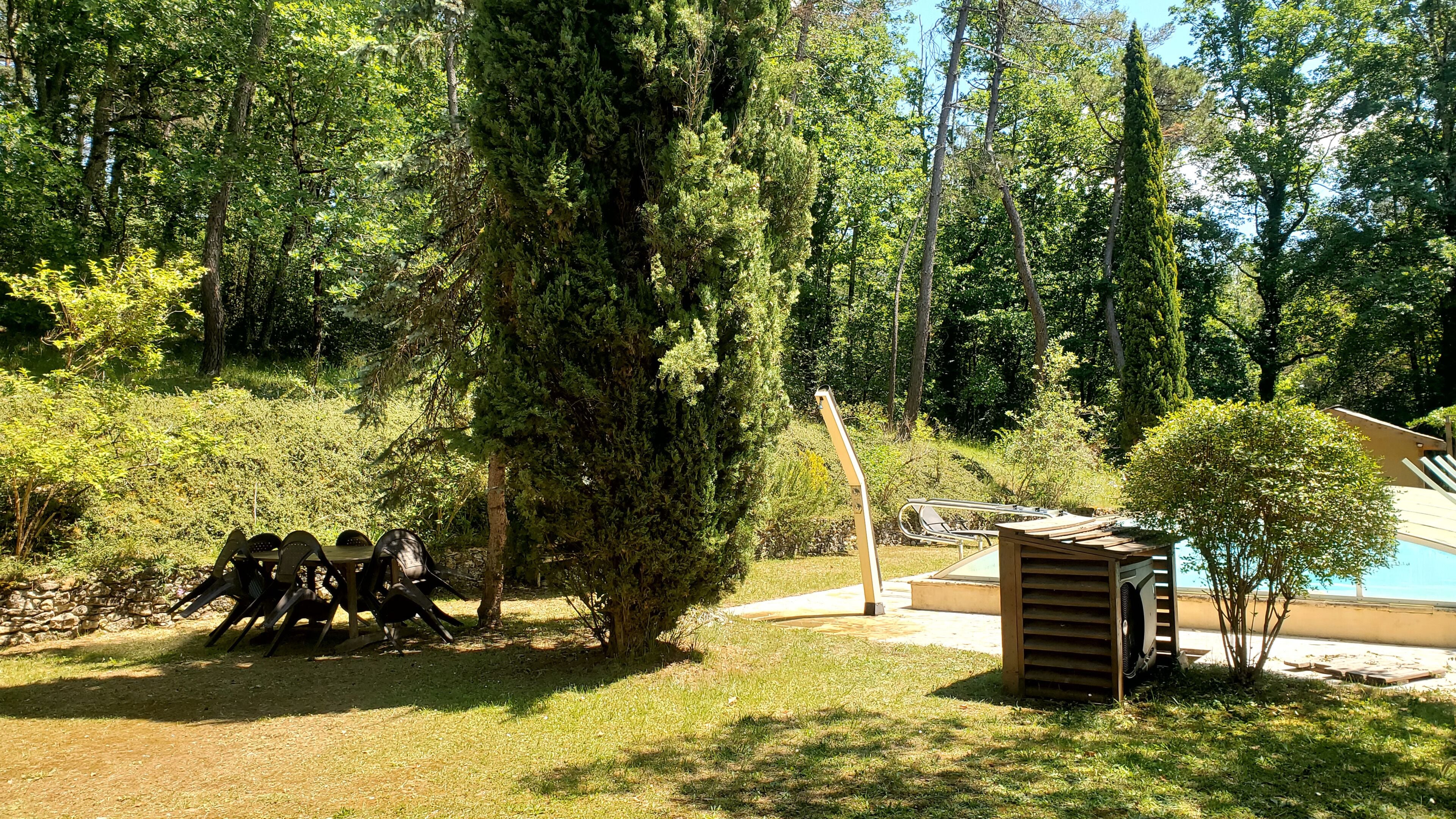 Un espace jardin agrémenté d’une petite construction en bois, peut-être un abri de jardin, entouré d’arbres et d’une pelouse.