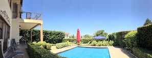 A pool area with a clear blue pool, surrounded by neatly trimmed hedges and a few lounge chairs.