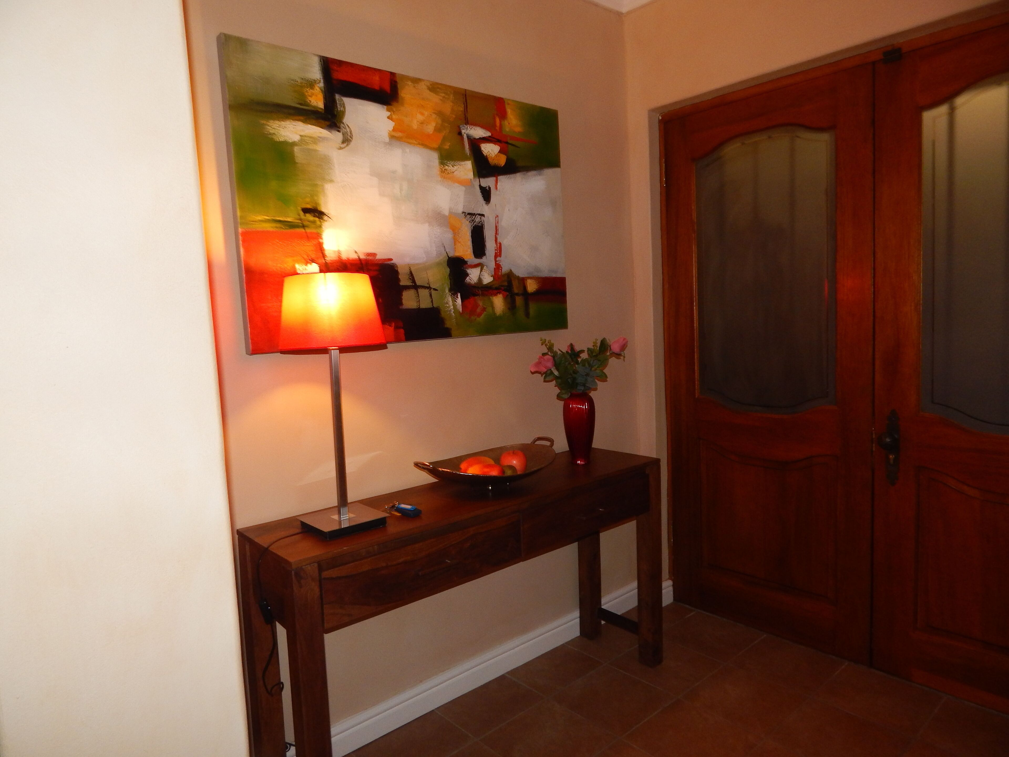 A wooden console table with a lamp, a vase with flowers, and a tray with fruit.