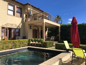 Una casa de dos pisos con piscina, un porche cubierto y un paraguas rojo.