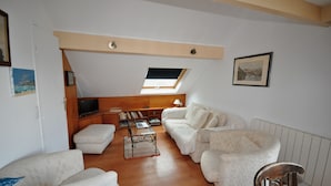 A spacious living room with a high ceiling, a skylight, a sofa set, a wooden coffee table, and a television on a wooden stand.