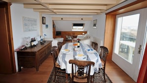 A dining room with a large table set for six, wooden chairs, a chandelier, and a view through a large window.