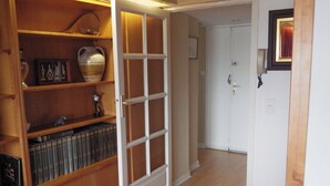 A hallway with wooden shelves containing books and decorative items, leading to a white door.