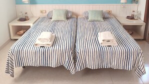 A double bed with striped bedding, two bedside tables with lamps, a framed picture of a coastal scene, and a tiled floor. - House with private pool and wi. fi (Coma-Ruga)