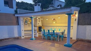 A swimming pool with a tiled deck, a covered patio area with a table and chairs, and a decorative wall with tiles and wall art. - House with private pool and wi. fi (Coma-Ruga)