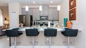 A modern kitchen with four bar stools, a central island, and a microwave above the island. - Dream Vacation Home Close to Disney SL4839 (Kissimmee)