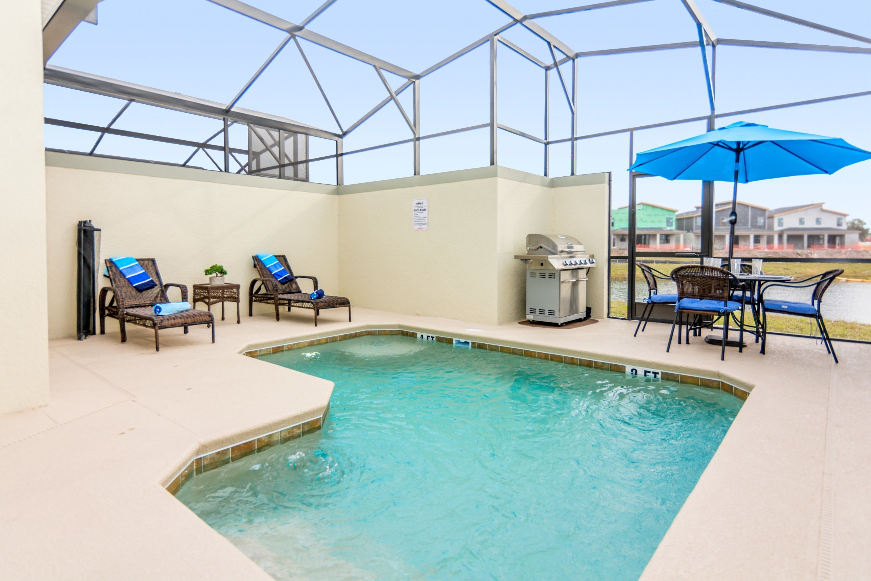 A covered outdoor swimming pool with lounge chairs and a grill area.
