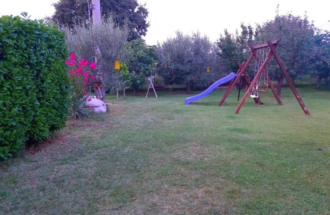 A grassy backyard with a swing set and a slide.