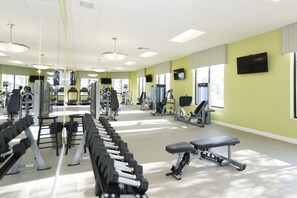 A gym with exercise equipment, a television, and large windows.