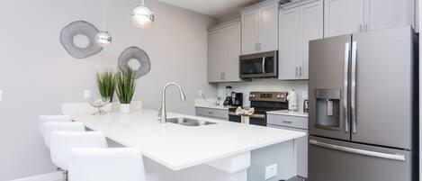 Une cuisine moderne dotée d’un îlot central, d’appareils électroménagers en acier inoxydable et de meubles blancs.