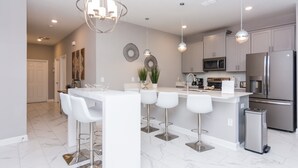 A modern kitchen with a central island, bar stools, stainless steel appliances, and pendant lighting.