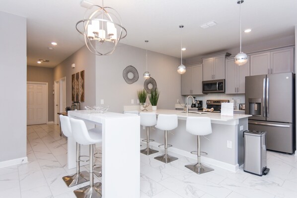 A modern kitchen with a central island, bar stools, stainless steel appliances, and pendant lighting.