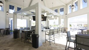 A spacious outdoor seating area with a bar and tables, large windows, and a high ceiling.