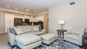 A modern living room with a sectional sofa, ottoman, and a small side table with a lamp.