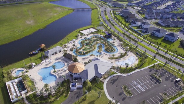 An aerial view of a resort with multiple swimming pools, a parking area, and a bridge over a body of water.