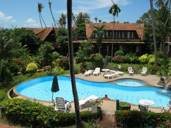 A resort with a large swimming pool surrounded by lounge chairs and a tropical garden.