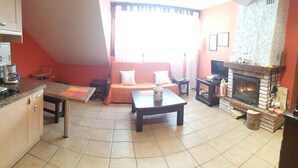 A cozy living area with a sofa, coffee table, fireplace, and kitchen area with a coffee machine.