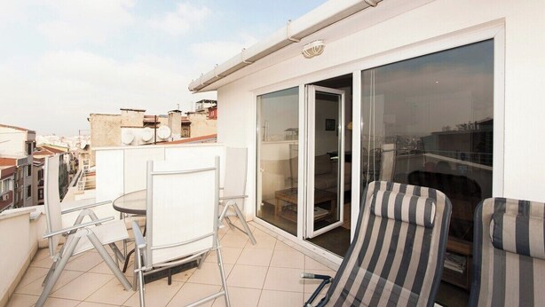A balcony with a glass door, a small table, and two striped chairs.