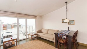 A living room with a sofa, a dining table with chairs, a coffee table, and a large window with a view of the outside.