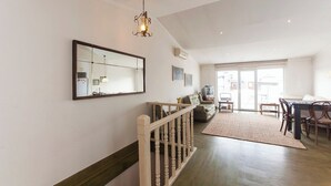 A spacious living area with a wooden floor, a dining table with chairs, a sofa, and a TV.