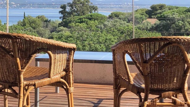 Deux fauteuils en osier sont placés sur une terrasse en bois, d’où l’on peut admirer un plan d’eau et la verdure environnante.