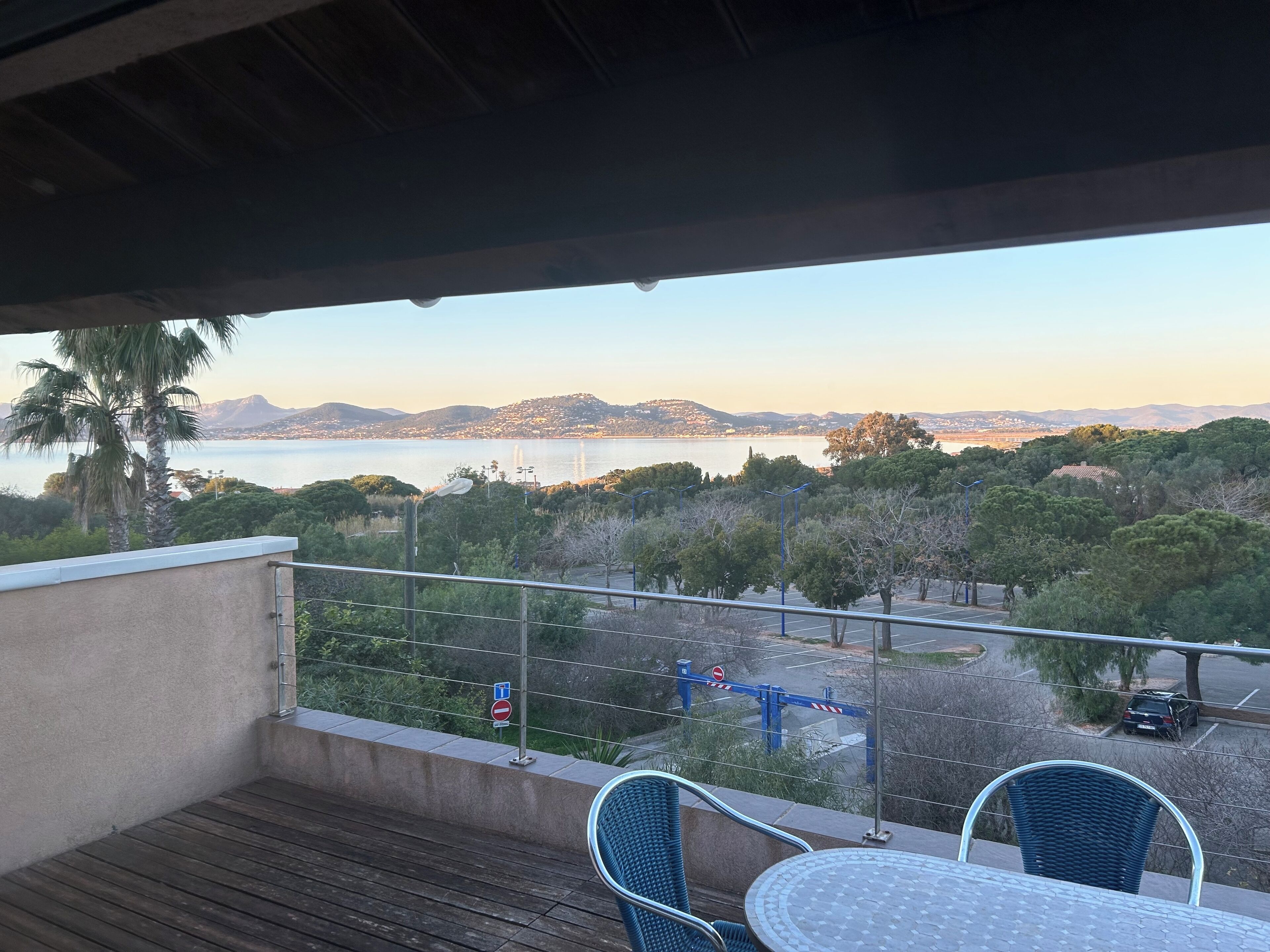 A balcony with a view of a body of water, trees, and distant hills.