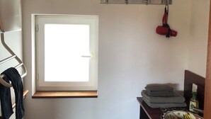Une petite pièce avec une fenêtre, un porte-manteau, une étagère avec des serviettes et un miroir.
