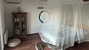 Une chambre à coucher avec un lit à baldaquin, une armoire en bois, une fenêtre ronde et un tabouret en osier.