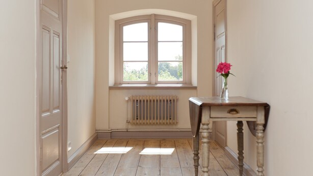 A hallway with wooden flooring, a radiator, a window, and a table with a vase. - Spacious and stylish in the monument to the Müritz, near the lake and golf course (Lexow)