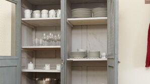 A grey metal cabinet with shelves containing white dishes, glasses, and a large metal bowl. - Spacious and stylish in the monument to the Müritz, near the lake and golf course (Lexow)