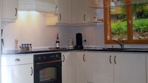A kitchen with white cabinets, a stove, and a window with a view of greenery. - Beautiful, spacious 12 person chalet, Portes du Soleil, France (Abondance)
