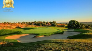 Campo de golf con cielo despejado, césped cuidado, bunkers de arena y una bandera en el green.