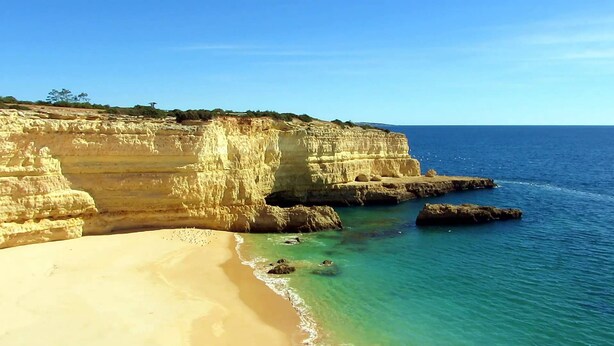 Un paisaje costero con playa de arena, mar azul transparente y acantilados rocosos.