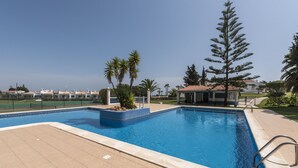 Una piscina con suelo de baldosas, rodeada de palmeras y un edificio con tejado de cerámica.