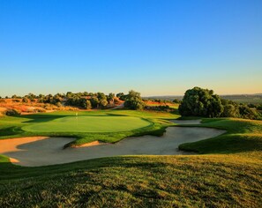 A golf course with a clear sky, well-maintained grass, sand bunkers, and a flag on the green.