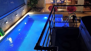Ein Swimmingpool mit einer Metallleiter, umgeben von einer Steinmauer und einem kleinen Garten.