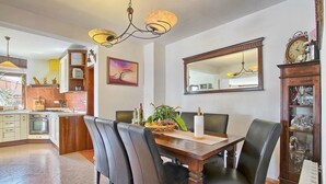 Een eetruimte met een houten tafel, zwarte stoelen, een kroonluchter en een keuken op de achtergrond.