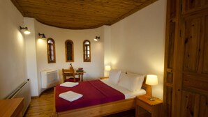 Een bed met houten frame, een rode deken en witte kussens, een nachtkastje met lamp, een houten stoel en een radiator.