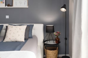A neatly arranged bedroom with a bed, bedside lamp, and a small table with a vase.