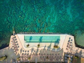 An aerial view of a resort with a pool, sun loungers, and a clear view of the surrounding turquoise waters. - Family-friendly,air-conditioned, quiet location, garden, barbecue, pets welcome. (Porec)